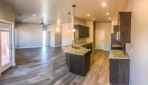 Kitchen with dark wood-style floors, a sink, light stone countertops, baseboards, and dark brown cabinetry
