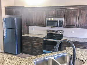 Kitchen with light stone counters, stainless steel appliances, dark brown cabinets, wood finished floors, and a sink