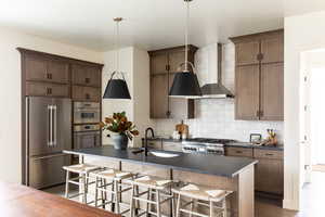 Kitchen with wall chimney range hood, dark countertops, stainless steel appliances, and a sink