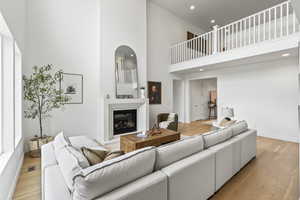 Living room with recessed lighting, a glass covered fireplace, light wood-style flooring, and a high ceiling