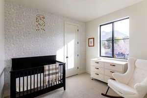 Bedroom with light colored carpet, wallpapered walls, a crib, and a mountain view