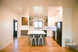 Kitchen featuring open shelves, a sink, black appliances, a kitchen bar, and white cabinetry