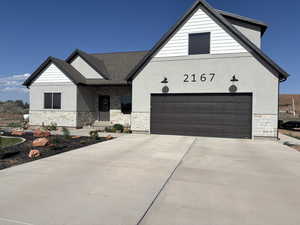 View of front of home featuring stone siding, stucco siding, driveway, and roof with shingles