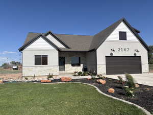 View of front of home featuring stone siding, concrete driveway, and a front lawn