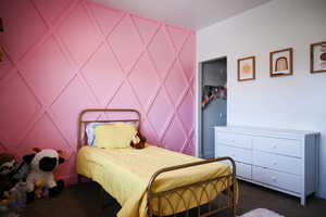 Bedroom featuring dark colored carpet and a decorative wall