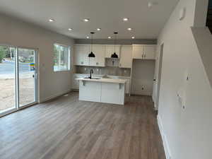 Kitchen with wood finished floors, a sink, decorative backsplash, an island with sink, and baseboards