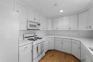 Kitchen with white cabinets, light wood finished floors, white appliances, and light countertops