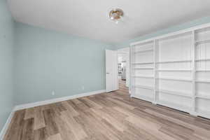 Unfurnished bedroom with stainless steel refrigerator with ice dispenser, wood finished floors, and baseboards
