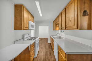 Kitchen with a sink, wood finished floors, white appliances, brown cabinets, and light countertops