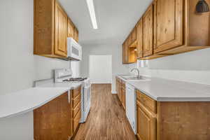 Kitchen with wood finished floors, a sink, brown cabinets, white appliances, and light countertops