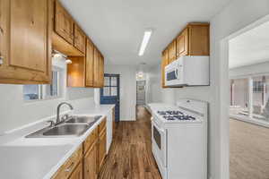 Kitchen featuring a sink, brown cabinets, white appliances, light countertops, and dark wood-type flooring