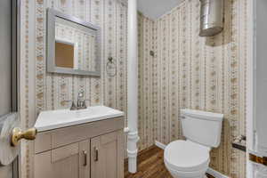 Half bathroom featuring baseboards, wood finished floors, toilet, and vanity