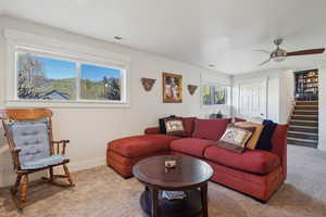 Carpeted living area with stairway, baseboards, visible vents, and ceiling fan