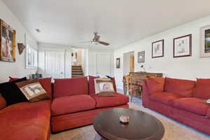Living room featuring carpet, visible vents, stairs, and ceiling fan