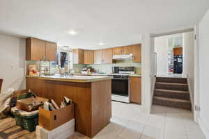 Kitchen with brown cabinets, gas range, light countertops, a peninsula, and under cabinet range hood