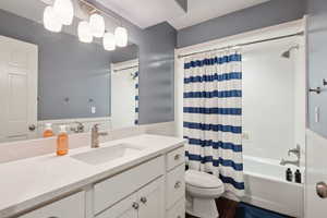 Bathroom with wood finished floors, wainscoting, vanity, toilet, and shower / bath combo with shower curtain
