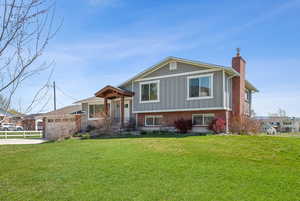 Split level home with a chimney, concrete driveway, brick siding, board and batten siding, and a front yard