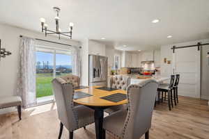 Dining room featuring a barn door, a notable chandelier, light wood finished floors, and recessed lighting
