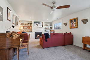 Carpeted living room with built in shelves, ceiling fan, a glass covered fireplace, and visible vents