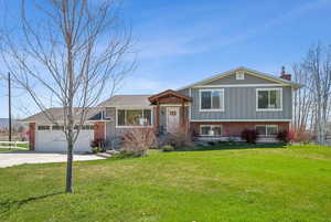 Tri-level home with a front lawn, a chimney, concrete driveway, brick siding, and an attached garage