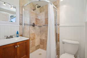 Full bath featuring a shower stall, toilet, vanity, and a wainscoted wall