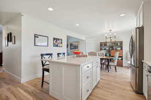 Kitchen with light wood finished floors, an inviting chandelier, freestanding refrigerator, a breakfast bar area, and white cabinetry