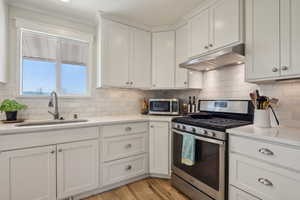 Kitchen with white cabinets, stainless steel appliances, under cabinet range hood, and a sink
