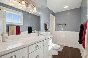 Bathroom with a wainscoted wall, wood finished floors, vanity, and toilet