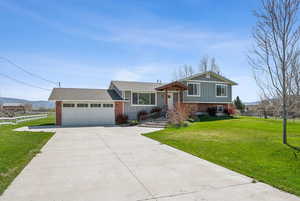 Tri-level home with concrete driveway, a front lawn, an attached garage, fence, and brick siding