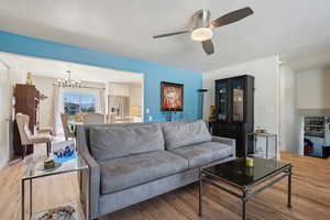 Living room with ceiling fan with notable chandelier and light wood-type flooring