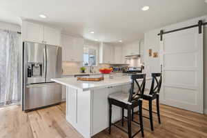 Kitchen with under cabinet range hood, a barn door, appliances with stainless steel finishes, and light wood finished floors