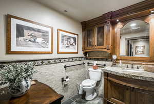 Bathroom featuring tile walls, toilet, vanity, and a wainscoted wall