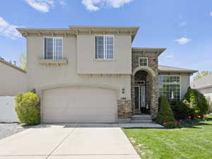 View of front of home with stone siding, an attached garage, and stucco siding