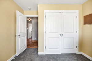 Bedroom with dark colored carpet, a closet, and baseboards