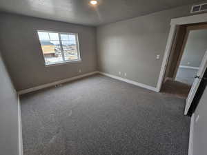 Spare room with dark carpet, baseboards, a textured ceiling, and visible vents