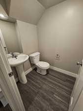 Half bathroom featuring a sink, toilet, vaulted ceiling, baseboards, and wood finished floors