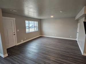 Interior space with a textured ceiling, baseboards, dark wood-style flooring, and visible vents