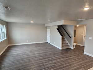 Unfurnished living room with stairway, dark wood-style floors, a textured ceiling, baseboards, and visible vents