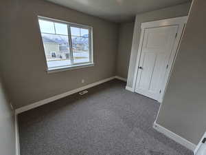 Unfurnished bedroom featuring dark carpet, baseboards, and visible vents
