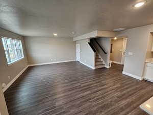 Unfurnished living room with stairway, a textured ceiling, dark wood-style floors, and visible vents
