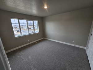Spare room featuring baseboards, dark colored carpet, a textured ceiling, and visible vents