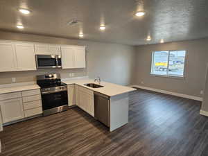 Kitchen featuring stainless steel appliances, a peninsula, a textured ceiling, a sink, and visible vents