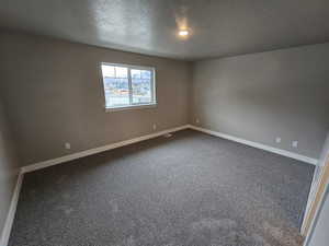 Empty room with baseboards, dark colored carpet, a textured ceiling, and visible vents