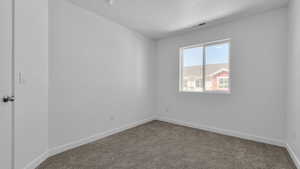 Empty room featuring baseboards, dark colored carpet, a textured ceiling, and visible vents
