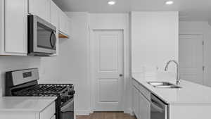 Kitchen with white cabinets, stainless steel appliances, a peninsula, light wood-style flooring, and a sink