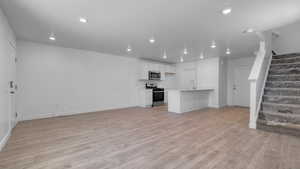 Unfurnished living room featuring baseboards, light wood finished floors, and stairs