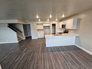 Kitchen with dark wood finished floors, baseboards, a peninsula, appliances with stainless steel finishes, and open floor plan