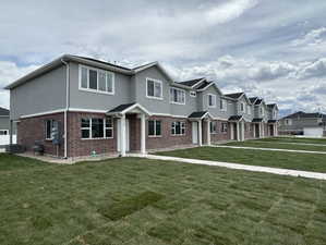 View of property with brick siding, stucco siding, a front yard, and central AC unit