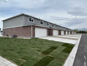 View of front facade with a front lawn, brick siding, cooling unit, and stucco siding