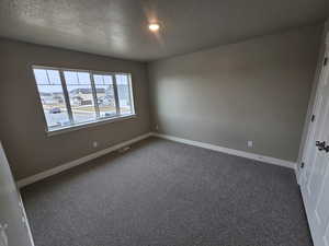 Empty room with visible vents, baseboards, dark carpet, and a textured ceiling